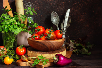 Fresh tomatoes and parsley, dill, garlic on a dark background in a rustic kitchen and wooden utensils still life with copy space