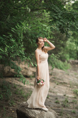 Beautiful luxury young bride inwedding dress standing near river with mountains on background