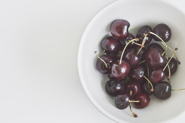 Fresh cherry berries in a white bowl on white table, top view, copy space