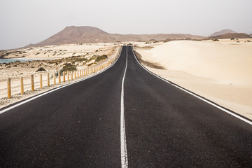 black dark asphalt road in the middle of the desert and sandy dunes of corralejo in fuerteventura. similar to african sahara landscape. sand on the road and travel and discover concept  © simona