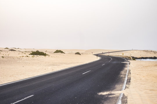 black dark asphalt road in the middle of the desert and sandy dunes of corralejo in fuerteventura. similar to african sahara landscape. sand on the road and travel and discover concept 