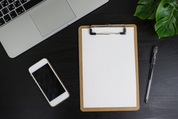 Still life, business, office supplies or education concept : Top view image of open notebook, clip board with blank pages, laptope, pen, phone and flower on wooden dark background, ready for adding or