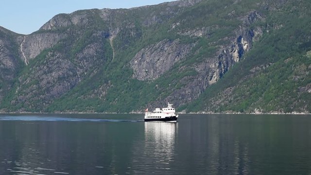 Small tour boat or ferry on a calm Norwegian fjord. Steep mountain sides in the background.