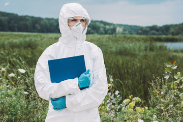 selective focus of female scientist in protective suit and googles holding clipboard in meadow