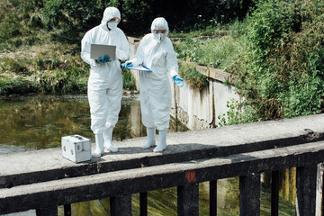 female scientist pointing on water of sewerage to male colleague with laptop