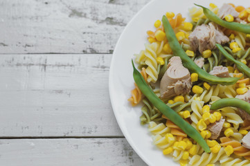 Pasta with tuna fish, sweet corn and green beans on gray wooden background. Balanced meal
