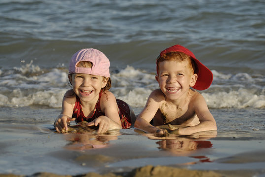 Two children are lying in the water at the beach and are having fun - Powered by Adobe