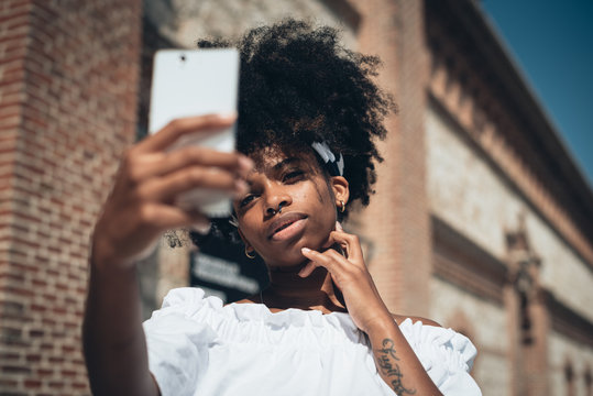 Trendy black woman taking selfie outdoors