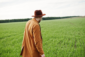 Stylish man in glasses, brown jacket and hat posed on green field.