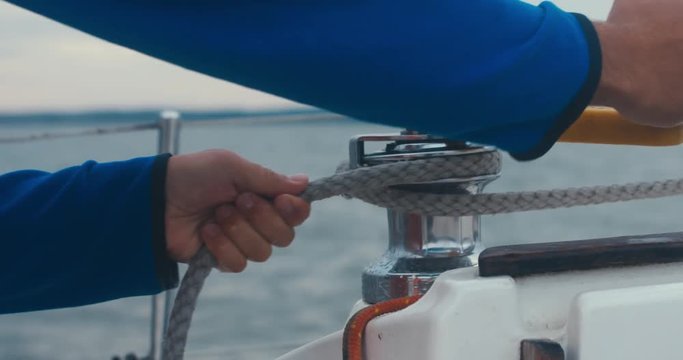 Male turning winch handle on yacht stern adjusting jib while sailing on a large lake, rainstorm in the background, bad rainy weather. 4K UHD 60 FPS SLO MO