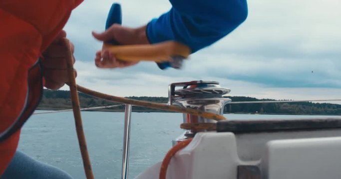Male turning winch handle on yacht stern adjusting jib while sailing on a large lake, rainstorm in the background, bad rainy weather. 4K UHD 60 FPS SLO MO