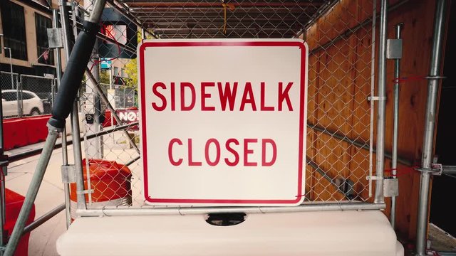 An sign reading "Sidewalk Closed" blocks the way in a construction zone downtown.