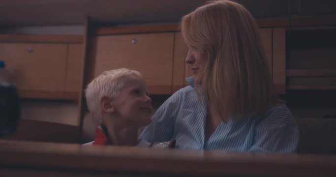 Beautiful young adult mother talking to her son in a cabin of yacht, family sailing on a lake. 4K UHD