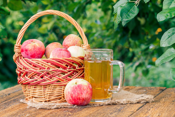 Just picked apples in a wicker basket and apple cider in glass goblet on wooden boards