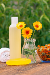 Bottle with skin care product and soap with marigold extract, towel, calendula flowers in a glass jar and bowl with dry flowers of calendula
