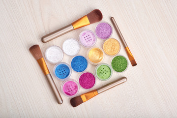 Naklejka premium Flat lay of arranged round tins with cosmetic bright dust glitters in composition with makeup brushes on wooden table