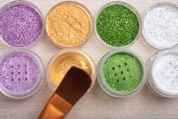 Top view in close-up of composed set of plastic cans with bright cosmetic glitters and makeup brush 