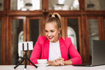 Young cheerful blogger in pink jacket happily recording new video for her vlog