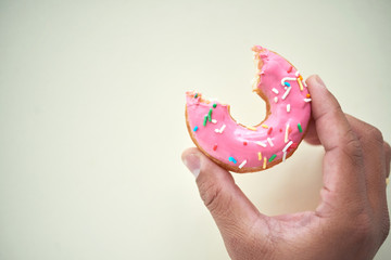 Crop person holding pink glazed doughnut in colorful sprinkles and with bite taken out against...