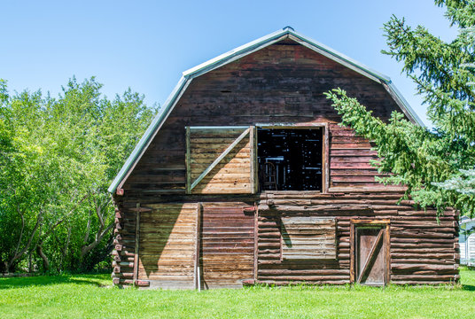 vintage wooden barn with open hayloft and gambrel roof surrounded by lush trees and greenery on a sunny summer day in Montana