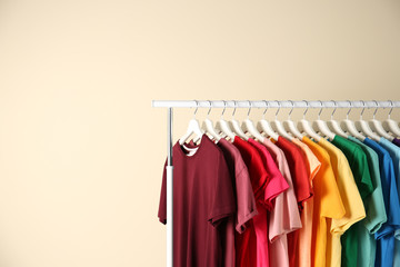 Many t-shirts hanging in order of rainbow colors on light background