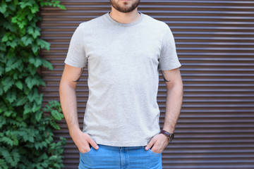 Young man wearing gray t-shirt near wall on street. Urban style