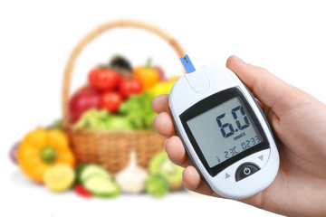 Woman holding digital glucometer and healthy food on white background