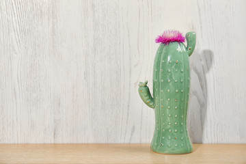 Trendy cactus shaped ceramic vase with flower on table against wooden background