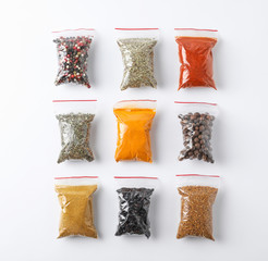 Plastic bags with different spices on white background, top view
