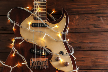 Guitar with fairy lights on wooden background, top view. Christmas music concept