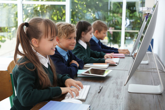 Little children in stylish school uniform at desks with computers - Powered by Adobe