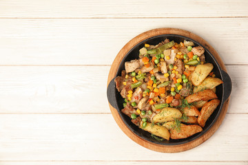 Pan with fried potatoes, meat and vegetables on wooden table, top view