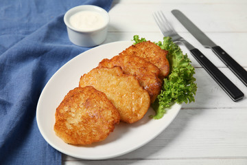 Plate with tasty potato fritters and sauce on wooden table