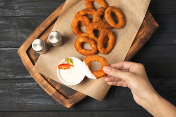 Woman dipping tasty onion ring into sauce at table