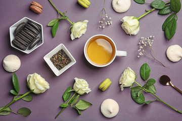 Flat lay composition with cup of tea, flowers and cookies on dark background