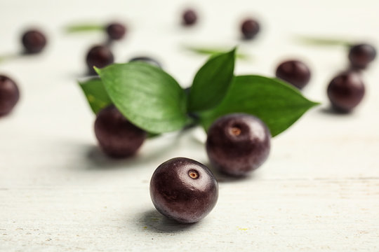 Fresh acai berries and leaves on wooden table, closeup