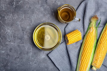 Flat lay composition with glassware of corn oil and fresh cobs on gray background