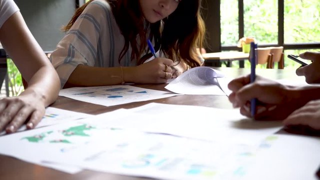 Close up of Young Asian people writing and preparing their presentation papers on the table (underexposed to show cinematic look)