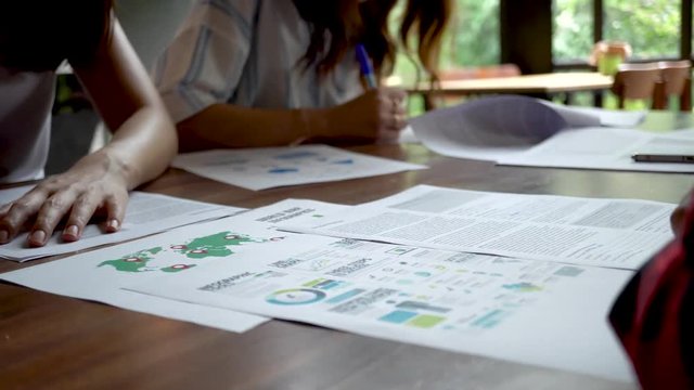 Close up of people writing and preparing their presentation papers on the table, using panning move technique (underexposed to show cinematic look)