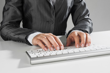 Closeup of businesswoman hand typing on keyboard with mouse on wood table