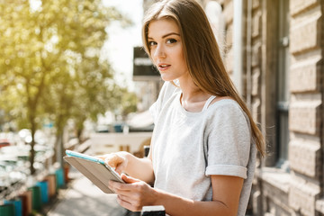 A light model of a girl holding a tablet in front of a sunny day street.