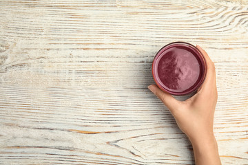 Woman holding glass of delicious acai juice on table, top view