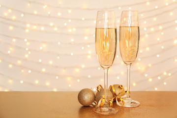 Glasses of champagne and Christmas balls on table against blurred lights