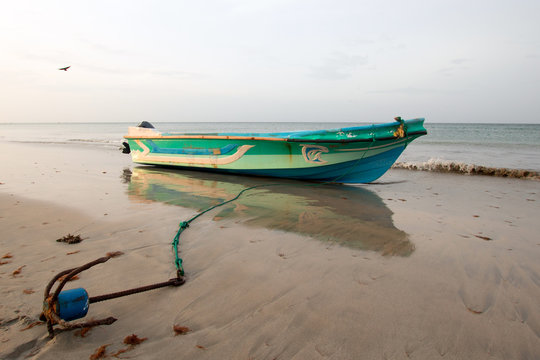Small fishing boat / panga with anchor at sunset on Nilaveli beach in Sri Lanka Asia