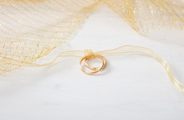 Two golden wedding rings tied with a golden ribbon on white wooden background