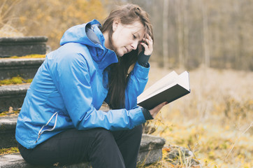 Girl ruffled her hair in thought while reading a book on the background of the autumn forest and...