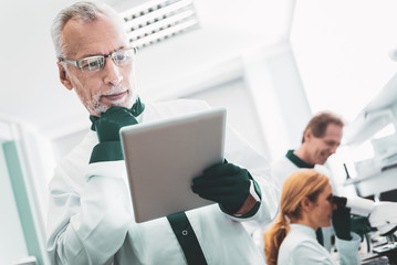 Modern technologies. Promising biotechnologist wearing gloves feeling amused while using modern technologies at work