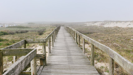 Fototapeta na wymiar Wooden footbridge of Costa Nova beach in a foggy morning. Aveiro, Portugal