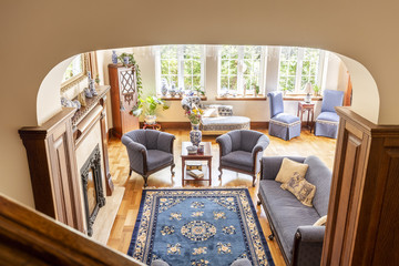 High angle of a rustical living room interior with a blue rug, armchairs, sofa and wooden floor