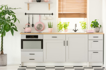 Pastel pink pan and kettle in a beautiful kitchen interior with simple, white cupboards and sink by...